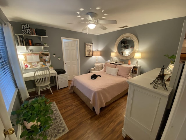 bedroom with dark wood-style floors, visible vents, ceiling fan, and built in desk