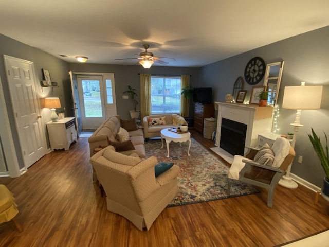 living room featuring a fireplace with flush hearth, a ceiling fan, baseboards, and wood finished floors