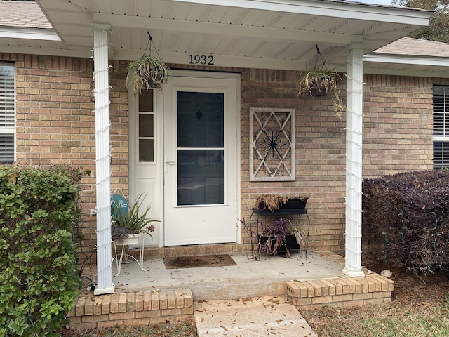 doorway to property featuring brick siding and roof with shingles