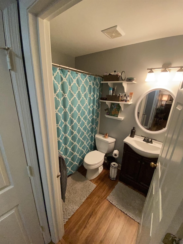 full bathroom with toilet, a shower with shower curtain, wood finished floors, vanity, and visible vents