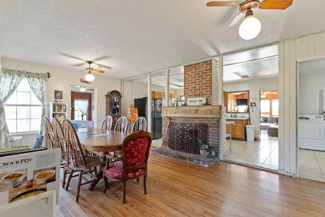 dining room with a textured ceiling, ceiling fan, light wood-type flooring, a brick fireplace, and washer / dryer