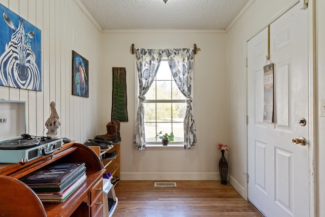 interior space featuring crown molding, visible vents, a textured ceiling, wood finished floors, and baseboards