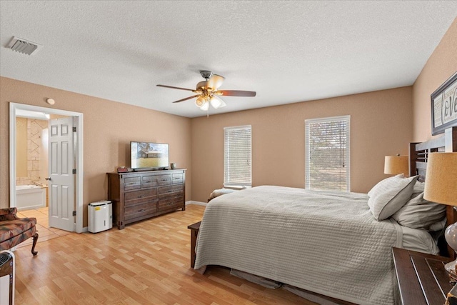 bedroom with a ceiling fan, visible vents, light wood-style flooring, ensuite bathroom, and a textured ceiling