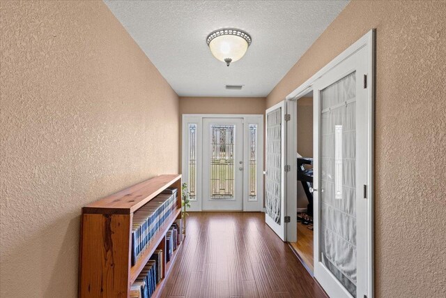 interior space with visible vents, dark wood finished floors, french doors, a textured ceiling, and a textured wall