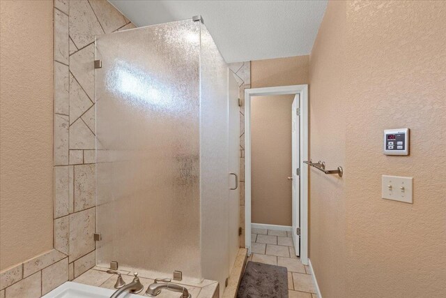 bathroom with a textured wall, a stall shower, a sink, and tile patterned flooring