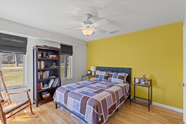 bedroom with a ceiling fan, wood finished floors, visible vents, and baseboards