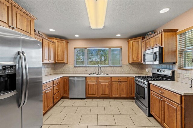 kitchen featuring brown cabinetry, a sink, stainless steel appliances, light countertops, and tasteful backsplash