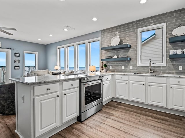 kitchen featuring stainless steel stove, a sink, open shelves, a peninsula, and wood finished floors