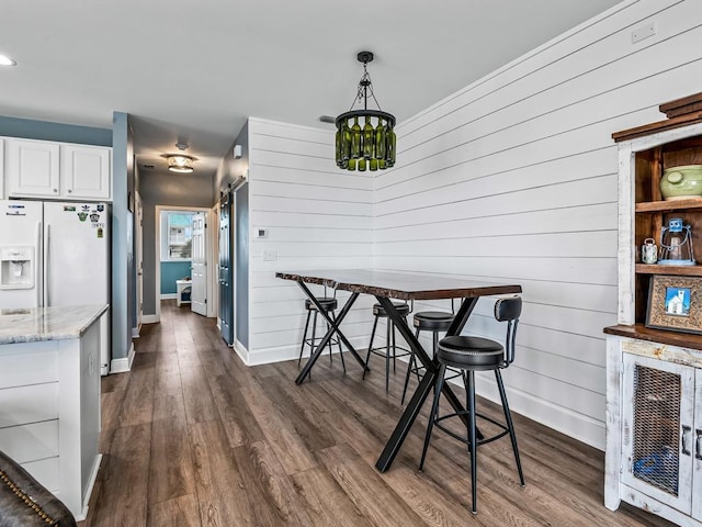dining area with baseboards, dark wood-style flooring, wood walls, and recessed lighting