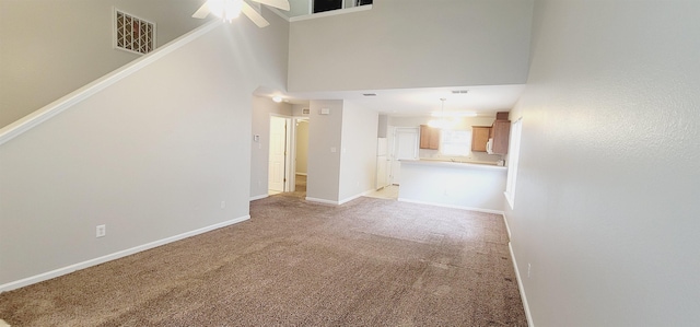 unfurnished living room with ceiling fan, a towering ceiling, and light colored carpet