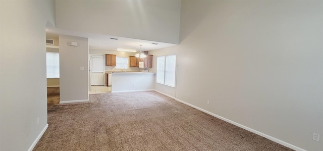 unfurnished living room featuring a chandelier, light colored carpet, and a high ceiling