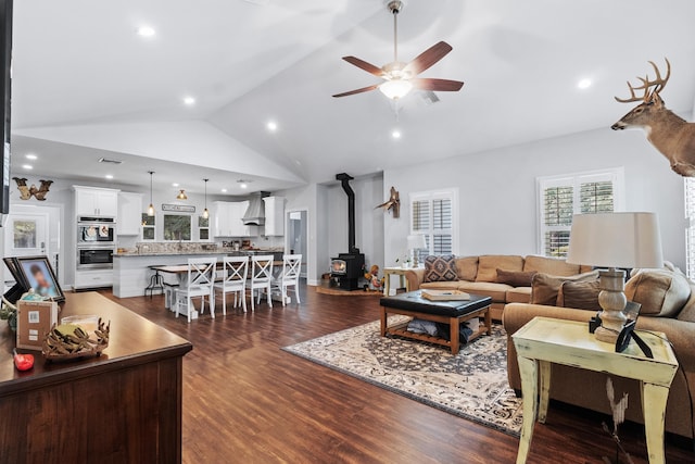 living room featuring dark wood-type flooring, ceiling fan, lofted ceiling, and a wood stove