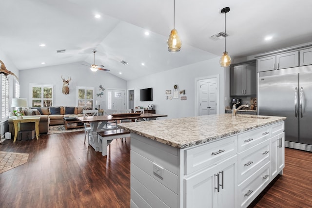 kitchen with sink, vaulted ceiling, hanging light fixtures, stainless steel built in fridge, and an island with sink