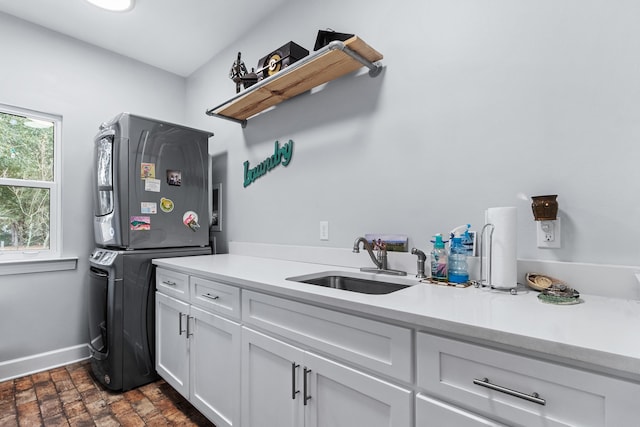 clothes washing area with cabinets, stacked washing maching and dryer, and sink