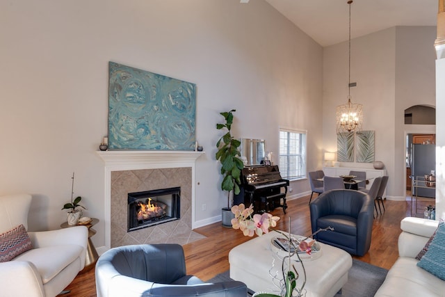 living room with a tiled fireplace, a notable chandelier, high vaulted ceiling, and hardwood / wood-style flooring