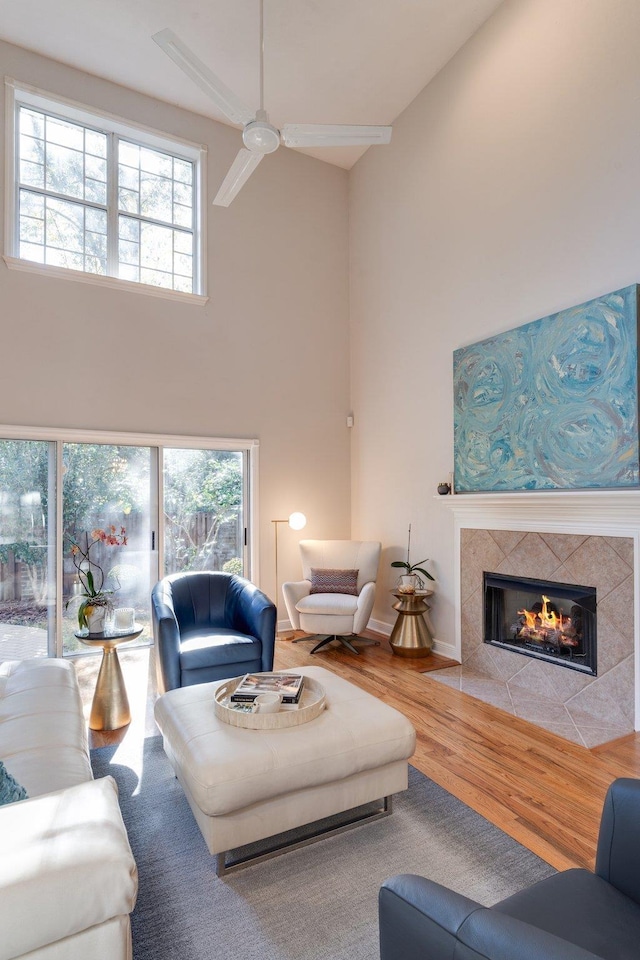 living room with a healthy amount of sunlight, a tiled fireplace, ceiling fan, and wood-type flooring