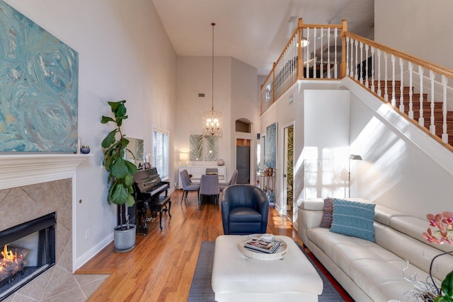 living room featuring a high ceiling, light wood-type flooring, a tiled fireplace, and an inviting chandelier