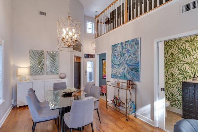 dining room featuring a towering ceiling, an inviting chandelier, and light hardwood / wood-style flooring