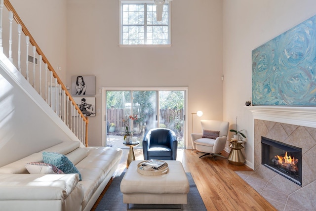 living room with a towering ceiling, a tiled fireplace, and light hardwood / wood-style flooring