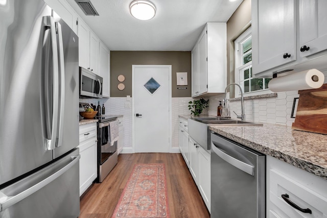 2809 Trebark Dr, Tallahassee, FL 32312 - kitchen with stainless steel appliances, wood finished floors, white cabinetry, and tasteful backsplash