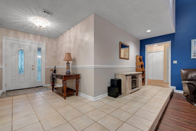 foyer with a textured ceiling, light tile patterned floors, visible vents, and baseboards