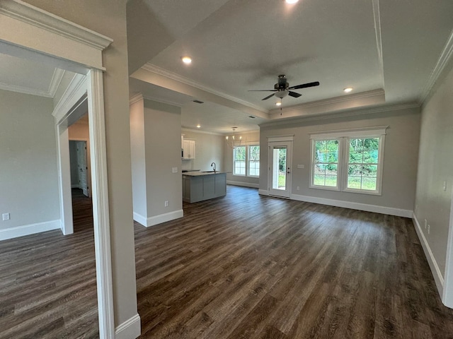 unfurnished living room featuring dark wood-type flooring, ceiling fan with notable chandelier, crown molding, and a tray ceiling