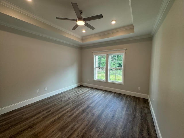 empty room featuring ornamental molding, dark wood-type flooring, ceiling fan, and a tray ceiling