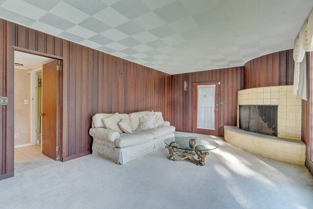 living room with a tile fireplace, light carpet, and wooden walls