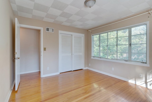 unfurnished bedroom with light hardwood / wood-style floors, multiple windows, and a closet