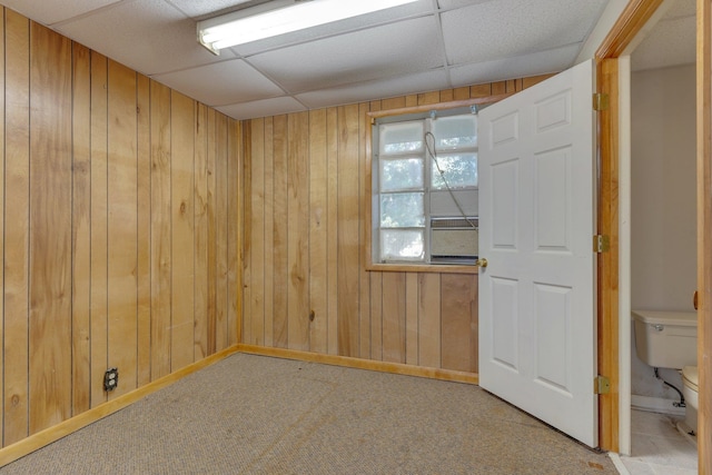 carpeted spare room with a paneled ceiling and wooden walls