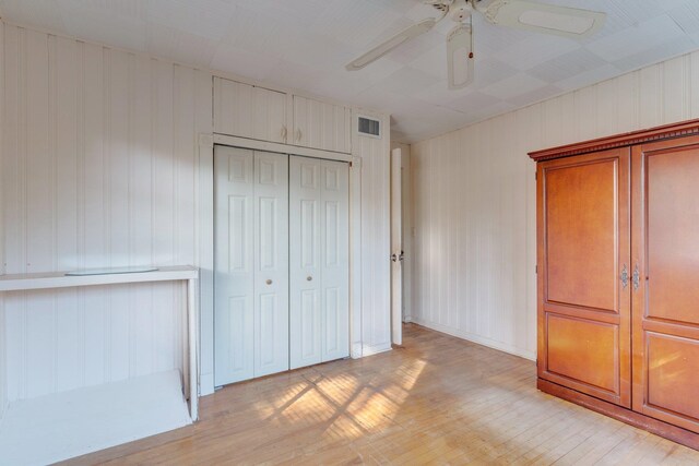 unfurnished bedroom featuring ceiling fan, wooden walls, a closet, and light wood-type flooring