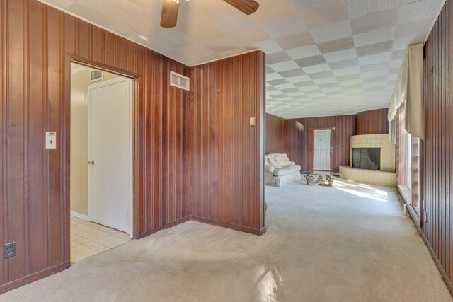 unfurnished living room with light colored carpet, wood walls, and ceiling fan