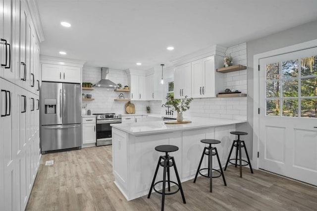 kitchen featuring pendant lighting, white cabinets, wall chimney range hood, appliances with stainless steel finishes, and kitchen peninsula