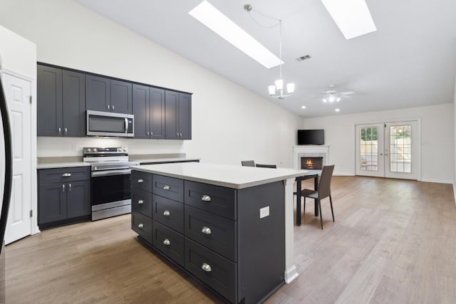 kitchen with pendant lighting, light hardwood / wood-style flooring, stainless steel appliances, vaulted ceiling with skylight, and a kitchen island