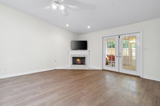 unfurnished living room with lofted ceiling, a tile fireplace, ceiling fan, french doors, and light wood-type flooring