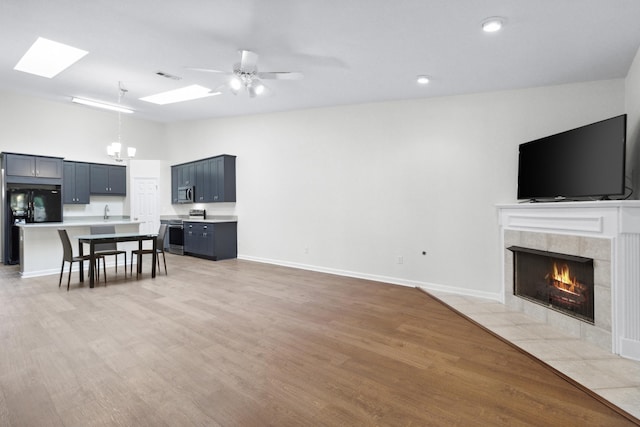 living room with lofted ceiling with skylight, light wood-type flooring, ceiling fan with notable chandelier, and a fireplace