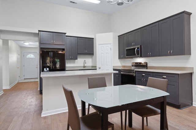 kitchen with sink, a high ceiling, a center island, stainless steel appliances, and light hardwood / wood-style flooring