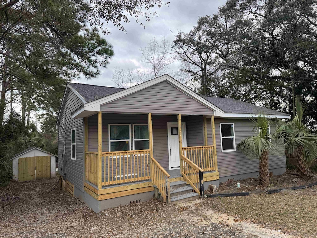 bungalow-style home featuring an outdoor structure, a storage unit, covered porch, and roof with shingles