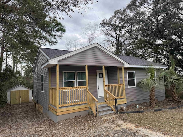 bungalow-style home featuring an outdoor structure, a storage unit, covered porch, and roof with shingles