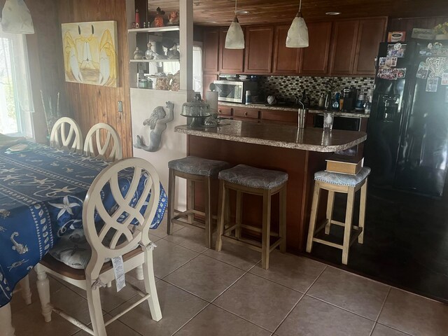 kitchen featuring tile patterned flooring, a breakfast bar, light stone counters, decorative light fixtures, and decorative backsplash