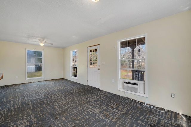 empty room with dark carpet, ceiling fan, cooling unit, and a textured ceiling