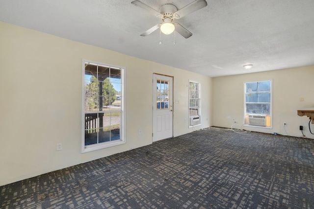 unfurnished living room featuring cooling unit, ceiling fan, dark colored carpet, and a textured ceiling