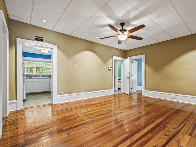 empty room featuring sink, a paneled ceiling, ceiling fan, and light wood-type flooring