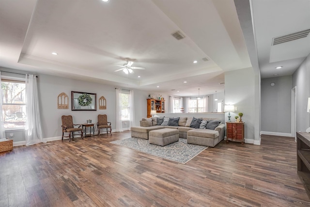 living area with a tray ceiling, dark wood-style floors, and visible vents