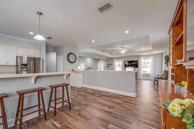 kitchen featuring visible vents, dark wood finished floors, a tray ceiling, stainless steel fridge with ice dispenser, and a kitchen bar