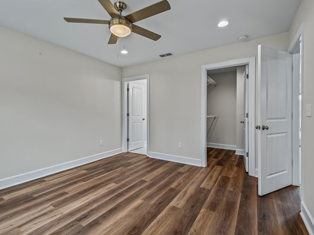 unfurnished bedroom with visible vents, baseboards, dark wood-style floors, a walk in closet, and a closet