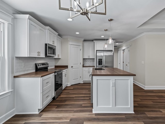 kitchen with wooden counters, appliances with stainless steel finishes, ornamental molding, white cabinets, and an island with sink