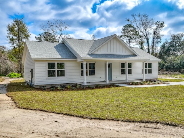 view of front facade with board and batten siding, a front yard, covered porch, and roof with shingles