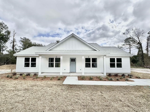 modern inspired farmhouse with board and batten siding, covered porch, a shingled roof, and a front lawn