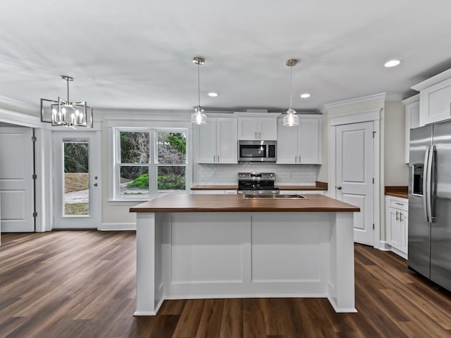 kitchen featuring white cabinetry, butcher block counters, appliances with stainless steel finishes, and decorative light fixtures